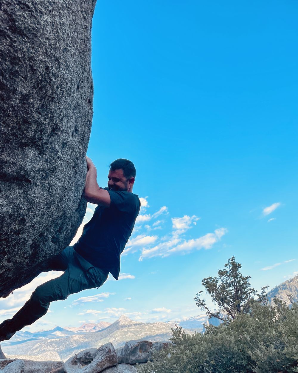Rob bouldering on a granite overhang with Sierra mountains behind him.